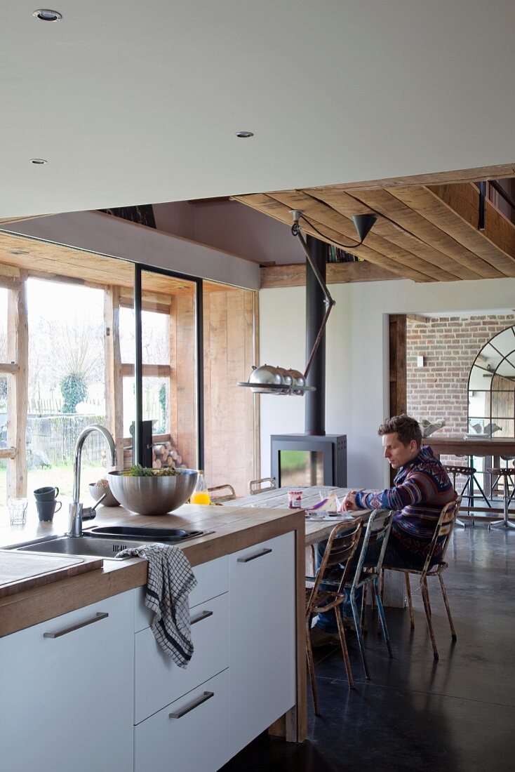 Offene Küche mit moderner Küchentheke, Mann am Essplatz, in renoviertem Landhaus