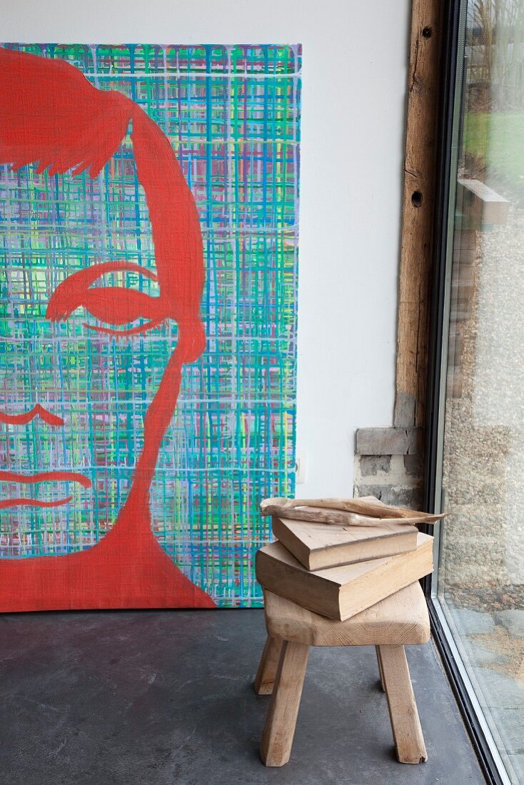 Bücher auf Holzhocker vor grossformatigem, modernem Männerportrait in Künstleratelier