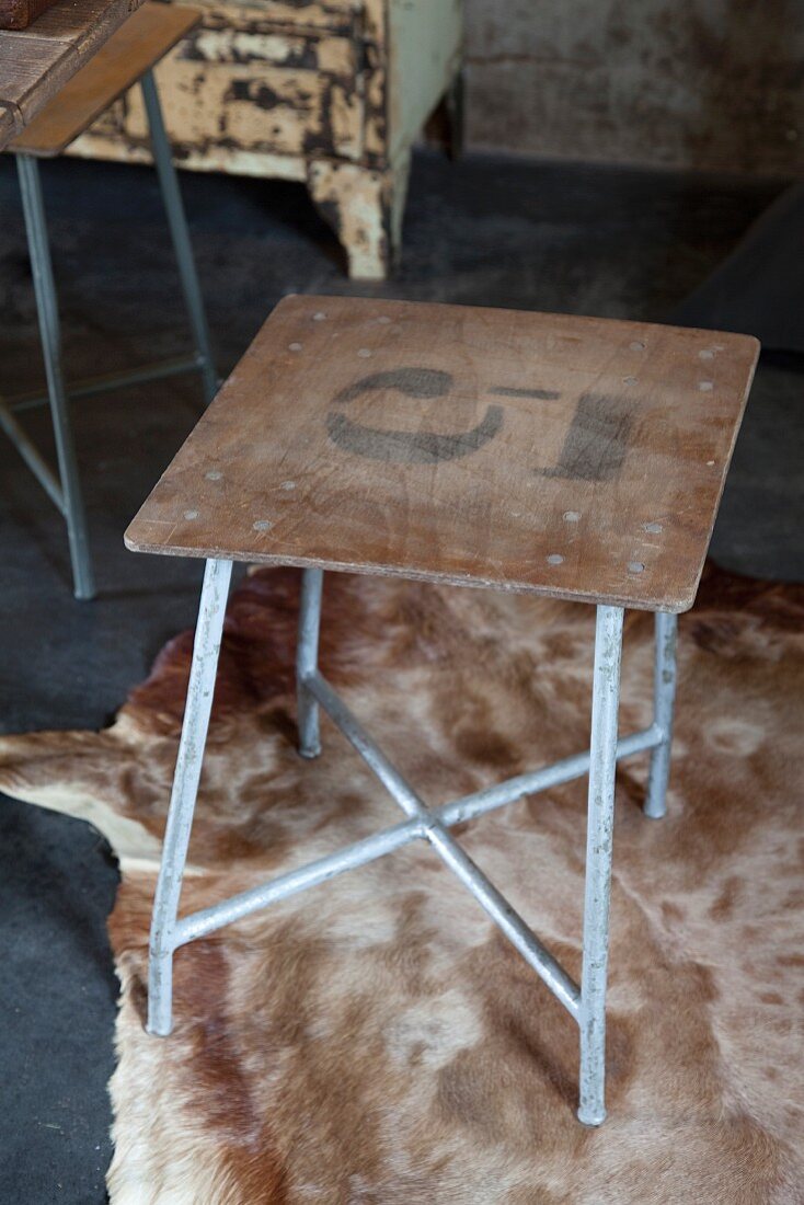 Vintage stool with number on simple wooden seat and metal frame on animal-skin rug
