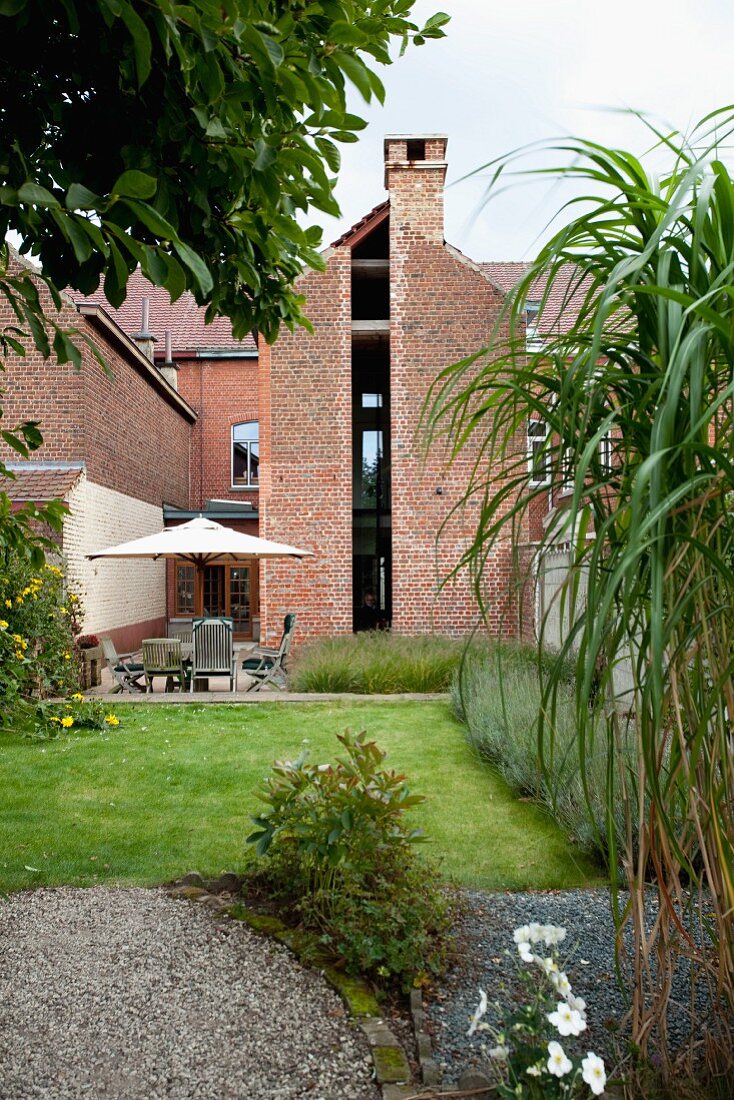 Garden with lawn adjoining terrace, restored brick façade with window slot running from ground to roof