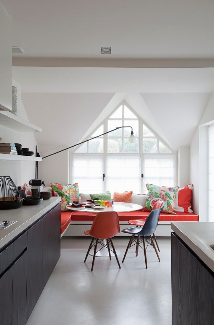 Open-plan kitchen with classic chairs at round table and L-shaped bench below gable window