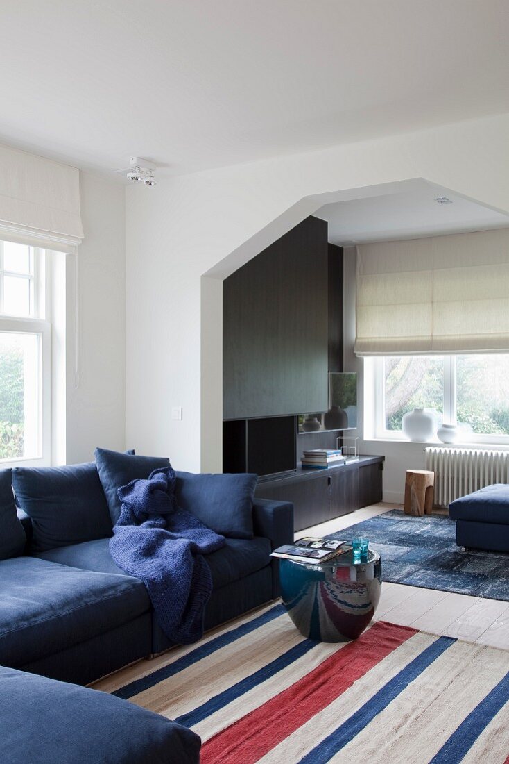 Sitzbereich mit blauem Sofa und bauchigem Beistelltisch auf gestreiftem Teppich, in grossräumigem Wohnzimmer