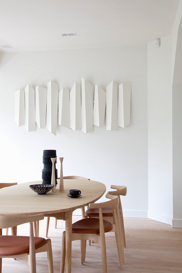 Moderner Essplatz mit Stühlen und Tisch aus hellem Holz, an Wand aufgehängtes Kunstobjekt in Weiß