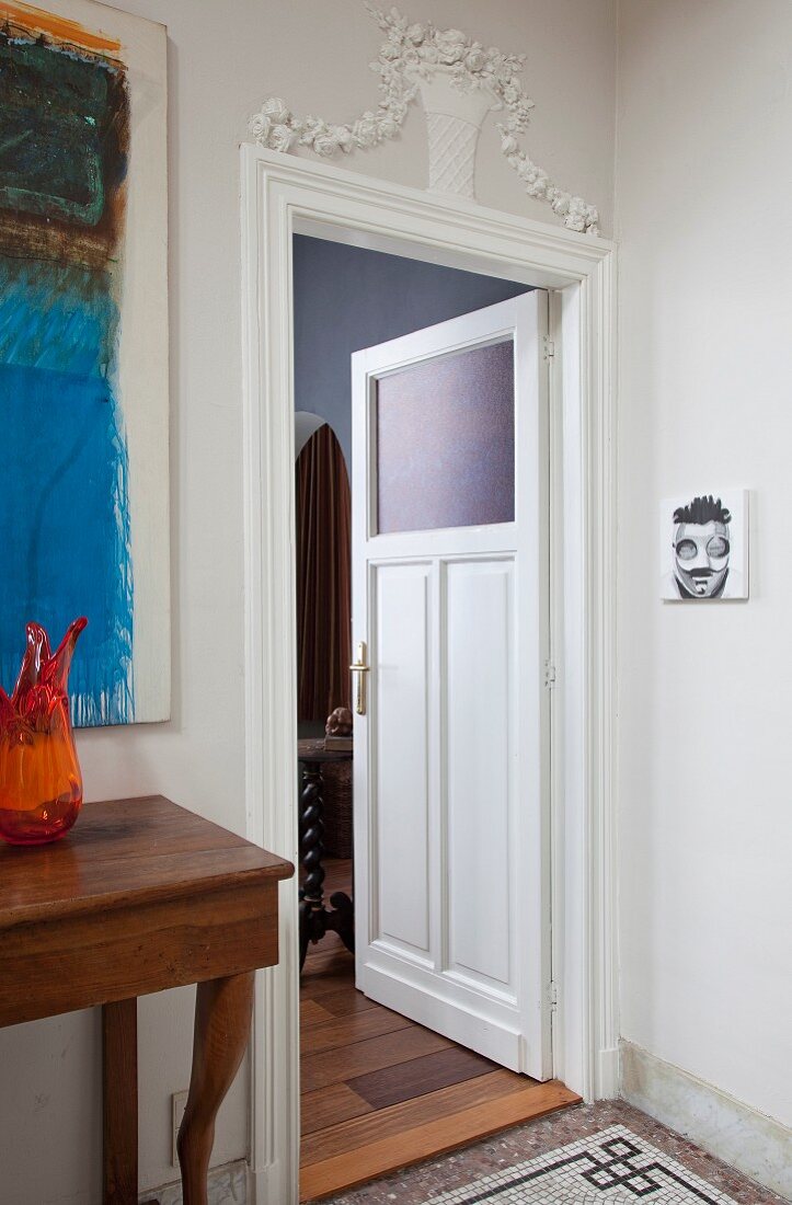 Offene Zimmertür mit Glasfüllung, über Türrahmen Stuckelement mit Blumenmotiv, seitlich Wandtisch