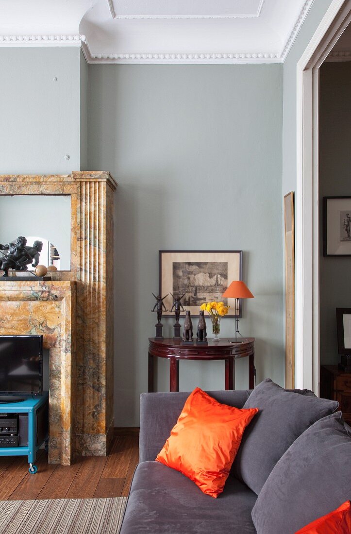 Dark grey couch with orange, silk scatter cushions in traditional living room with grey-painted wall