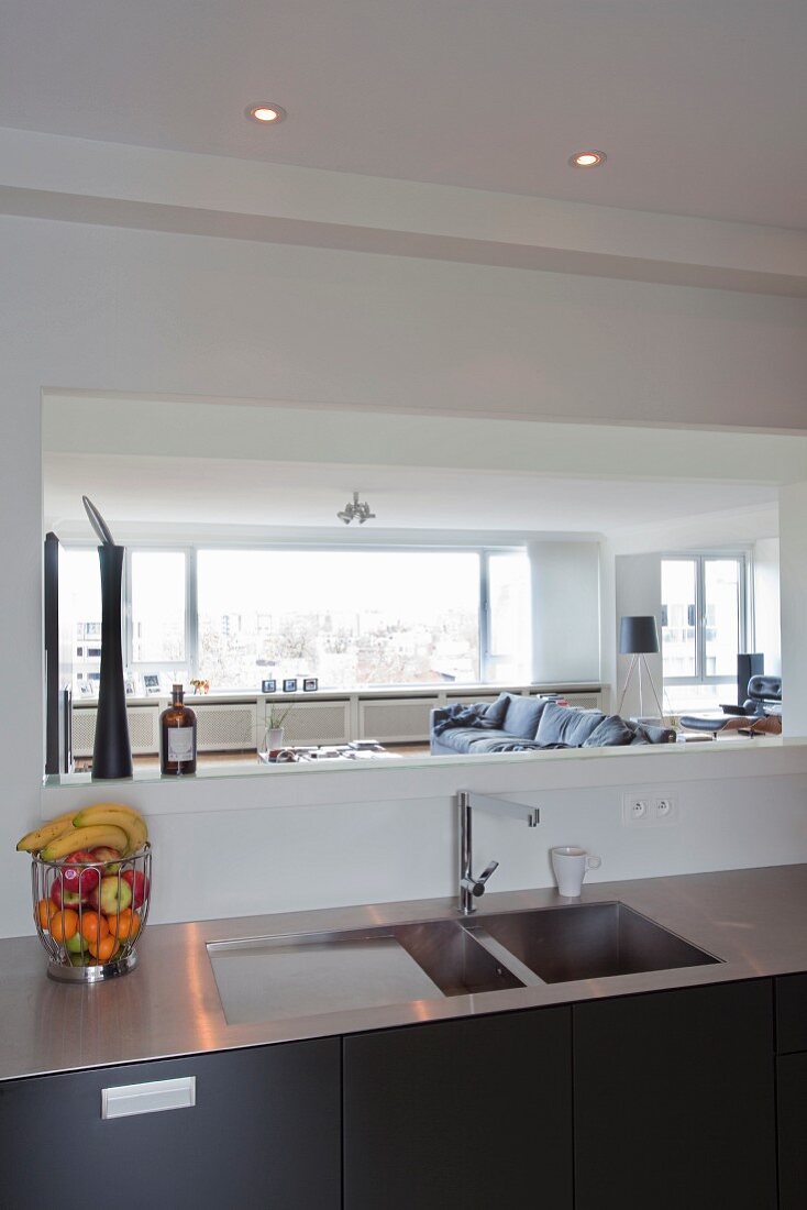 Aperture in wall above stainless steel worksurface with integrated sink; view into living space