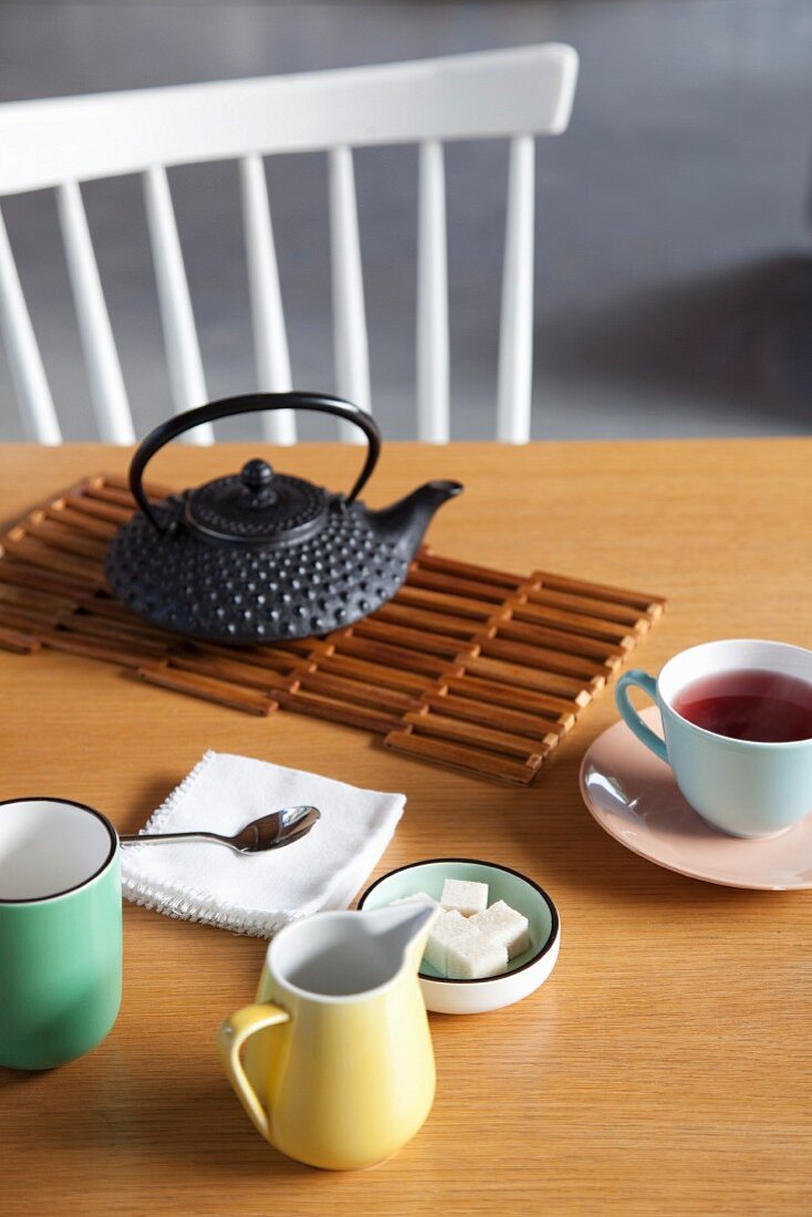 Tea service; pastel porcelain crockery and cast iron teapot on wooden table