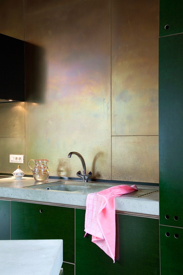 DIY kitchen counter with green cabinets, concrete worksurface and back wall clad in brass panels