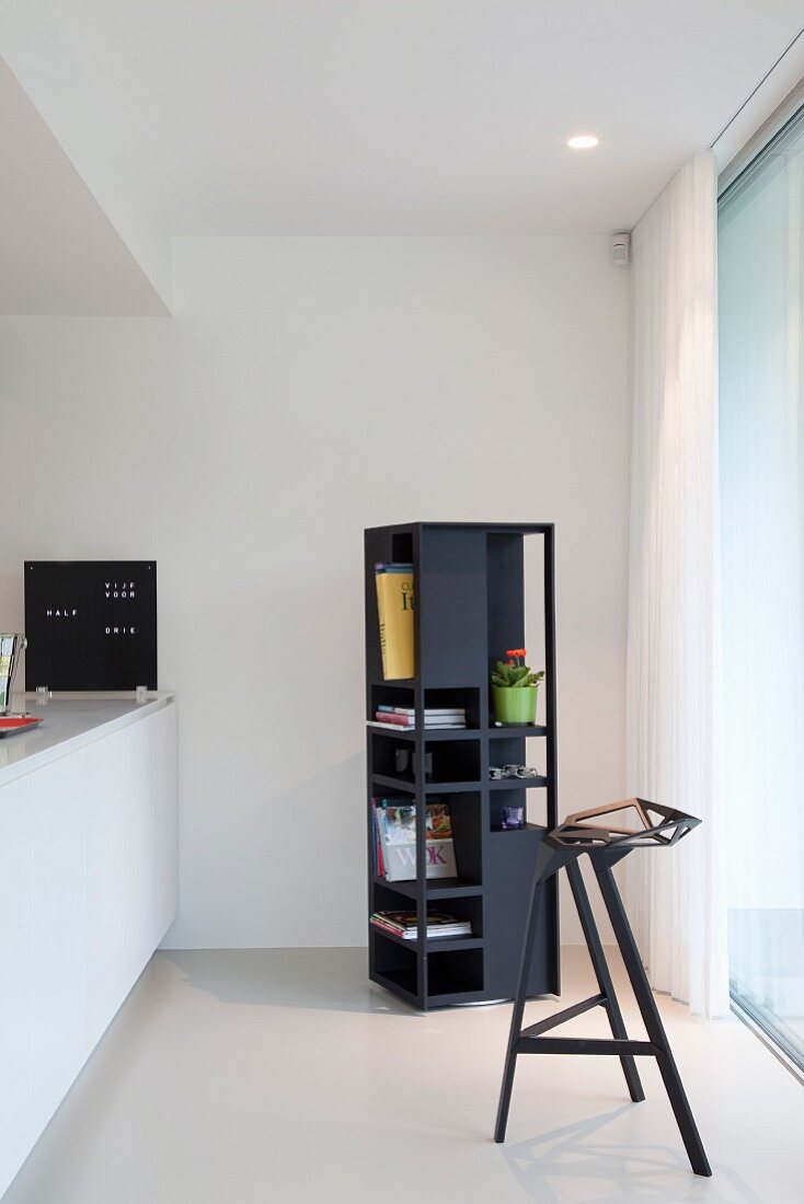 Rectangular, rotating shelving and black, designer bar stool next to white kitchen counter
