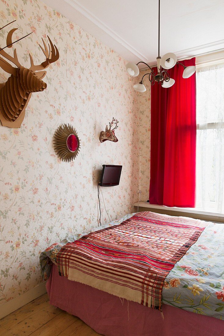 Schlichtes Doppelbett mit Tagesdecke, Tiertrophäen und Fernseher an Blumentapete