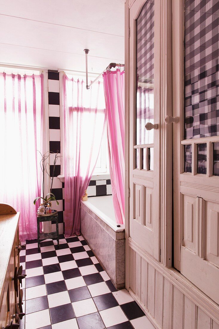 Vintage Bad mit Schachbrettmuster auf Boden und an Wand, rosa Vorhang am Fenster, seitlich eingebauter Schrank, weiss lackiert