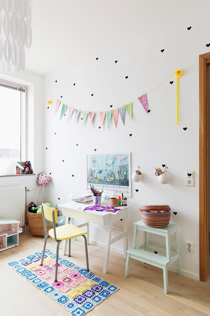 Gelber Stuhl vor weißem Schreibtisch, an Wand herzförmige Sticker und Wimpelkette im Kinderzimmer