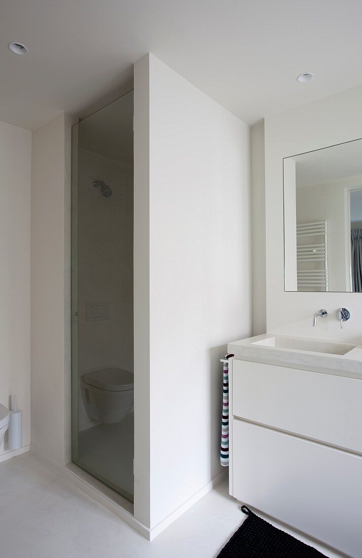 Detail of washstand with white base unit next to shower cubicle with masonry wall and glass door