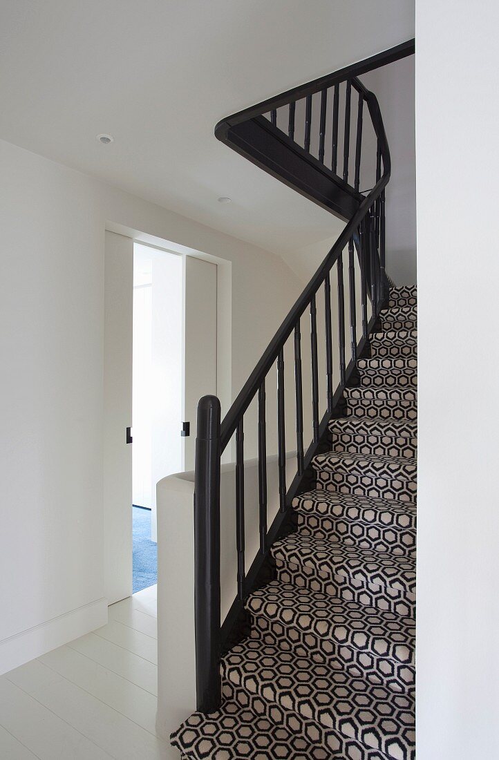 Staircase with black balustrade and black and white, geometric carpet in stairwell