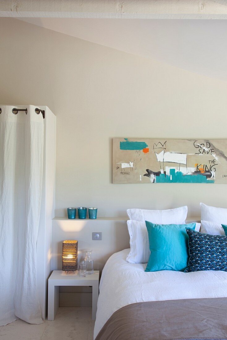 Modernes Bild über Doppelbett; gemauerte Ablage und Abmauerung als Schrank mit weißem Vorhang