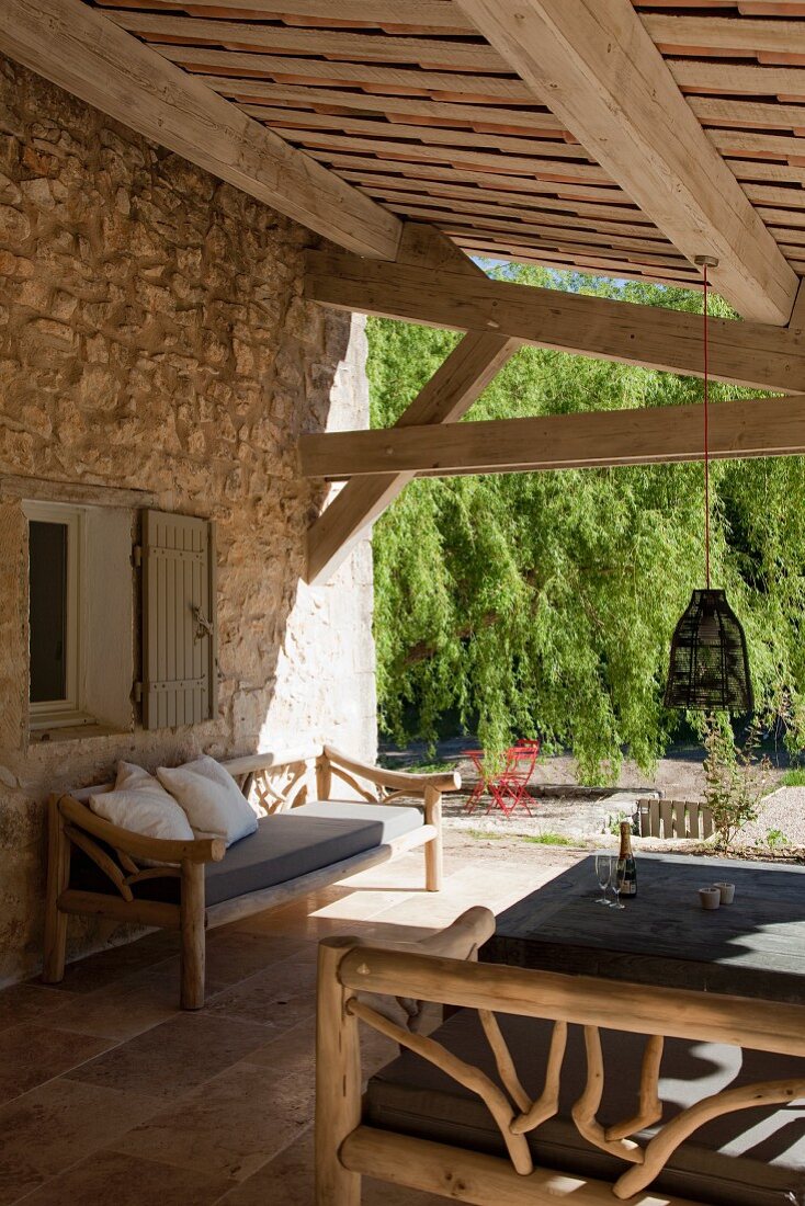 Outdoor Möbel aus Rundhölzern auf überdachter Terrasse vor provenzalischem Natursteinhaus