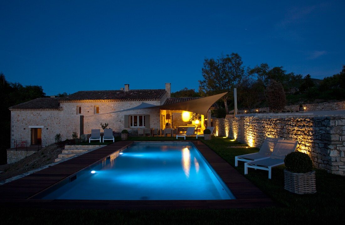Abendstimmung am beleuchteten Poolbereich vor traditionellem, renoviertem Landhaus