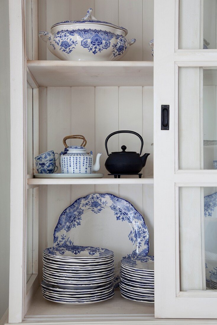 Blue and white plates, tureen and Oriental teapots in glass-fronted cabinet with open sliding door