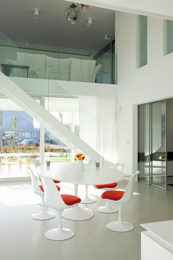 Tulip Table mit passenden Stühlen in Weiß und rote Sitzpolster vor Treppenaufgang in zeitgenössischem Wohnhaus