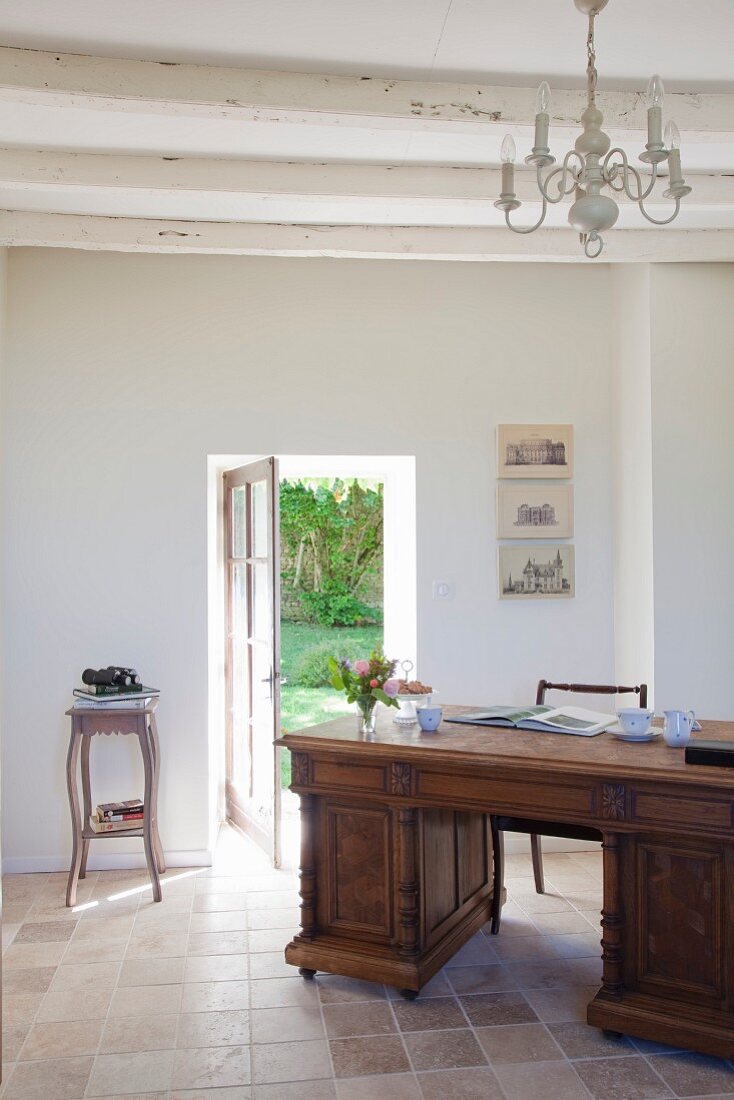 Antique desk in simple room with terracotta floor and white, wood-beamed ceiling