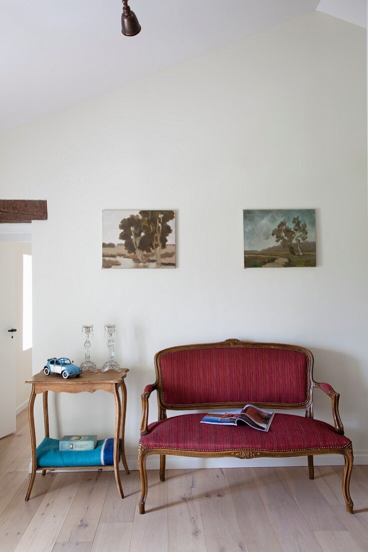 Rokoko Sitzbank mit rotem Bezug und Beistelltisch, darüber Landschaftsbilder an Wand