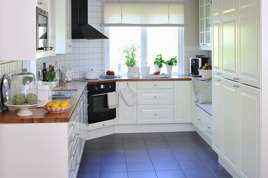 weiße Landhausküche mit Küchenzeile übereck auf dunklem Fliesenboden
