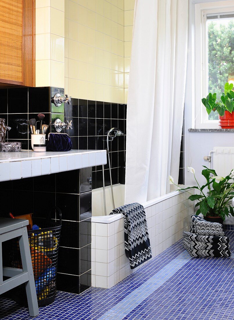 Tiles in mixture of colours and formats in bathroom; bathtub with shower curtain, masonry washstand and towels