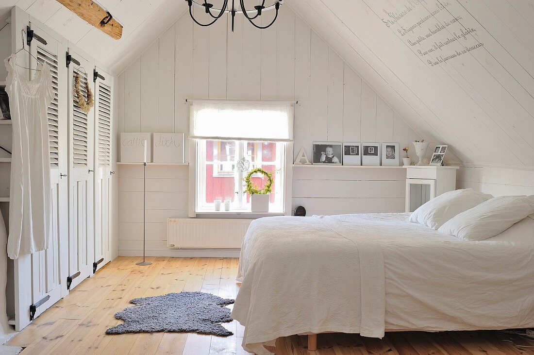Einfaches weißes Landhausschlafzimmer im Dachgeschoss mit Einbauschrank, naturbelassenem Dielenboden und skandinavischem Vintage Flair