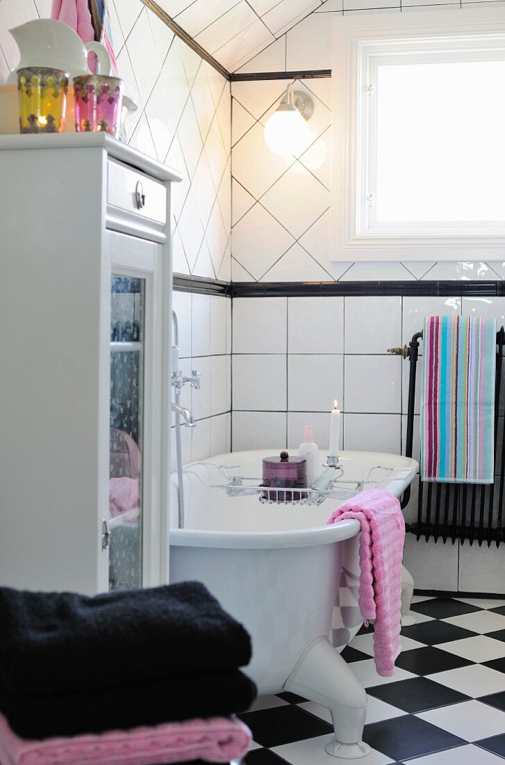 Free-standing bathtub with lit candle on bath rack in black and white country-house bathroom
