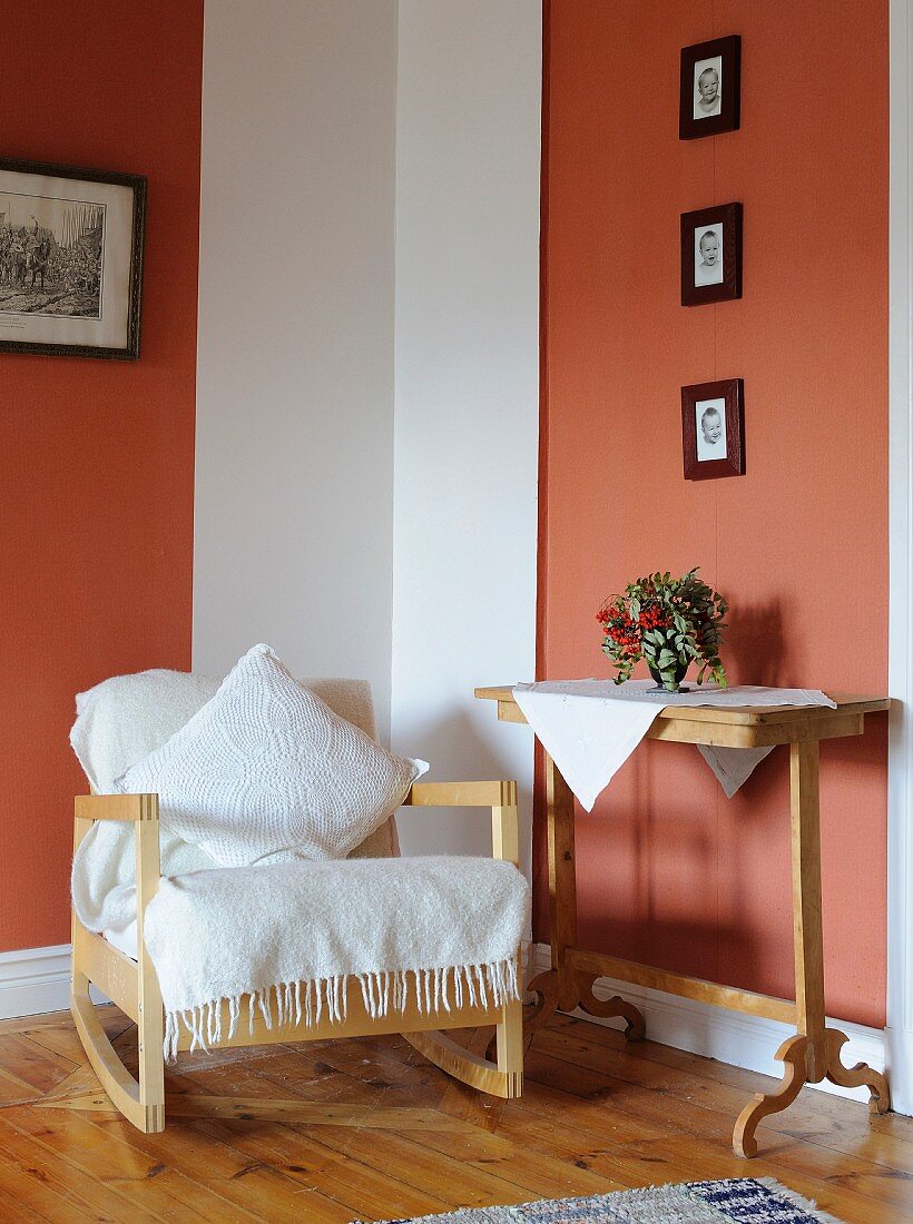 Pale, Scandinavian rocking chair, vintage console table and framed photos of children on terracotta wall panels in comfortable reading corner