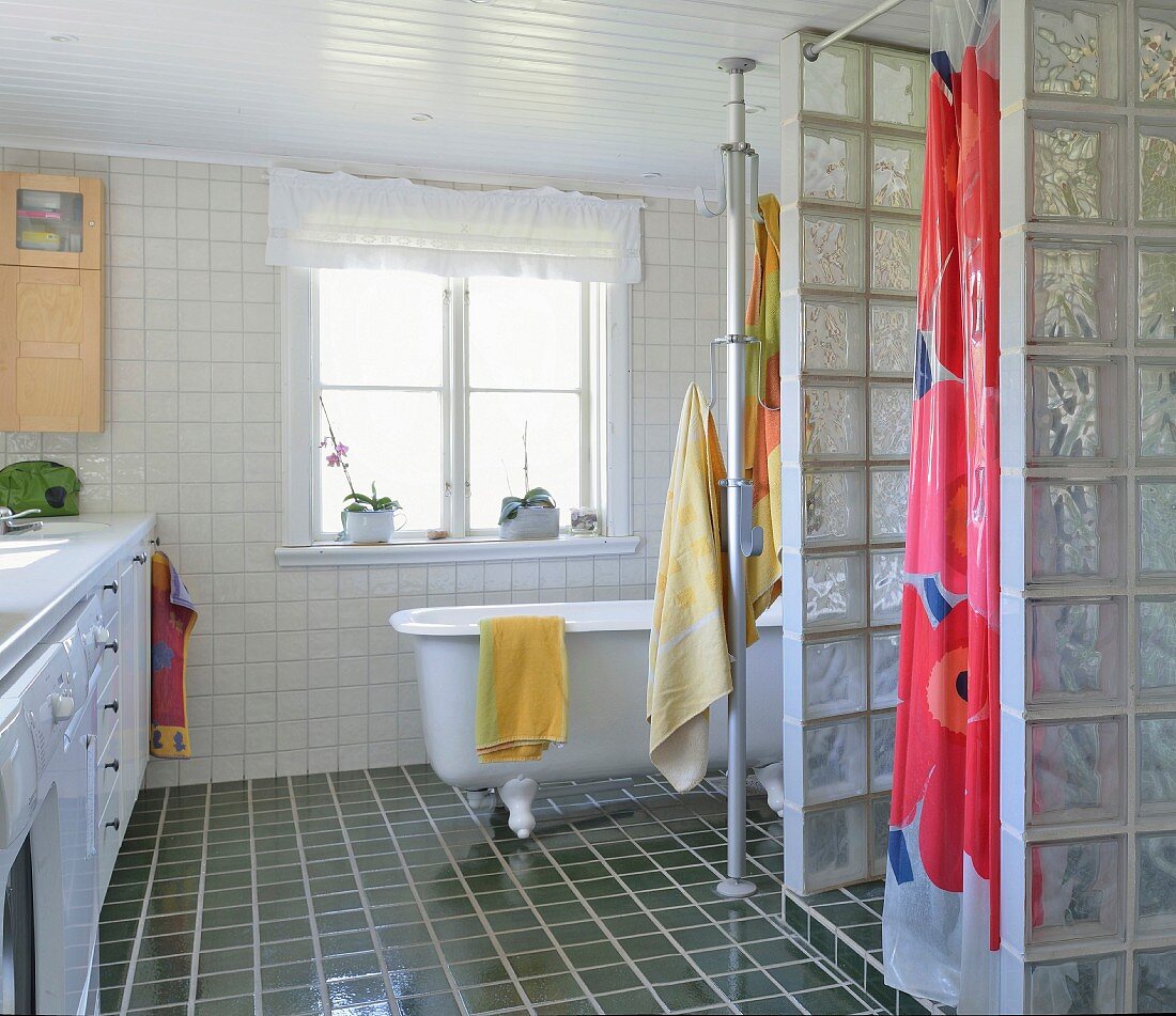 Duschbereich mit Glasbausteinwand, im Hintergrund freistehende Vintage Badewanne auf dunklem Fliesenboden