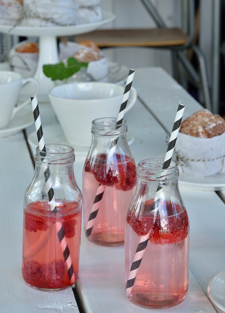 Himbeerdrink in drei Glasflaschen mit scharz-weißem Trinkhalm auf gedecktem Gartentisch