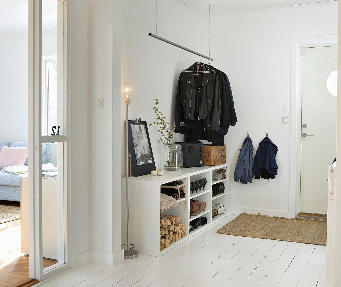Weißer Flurbereich mit offenem Schuhregal, abgehängter Garderobenstange und Stehleuchte in skandinavischem Ambiente