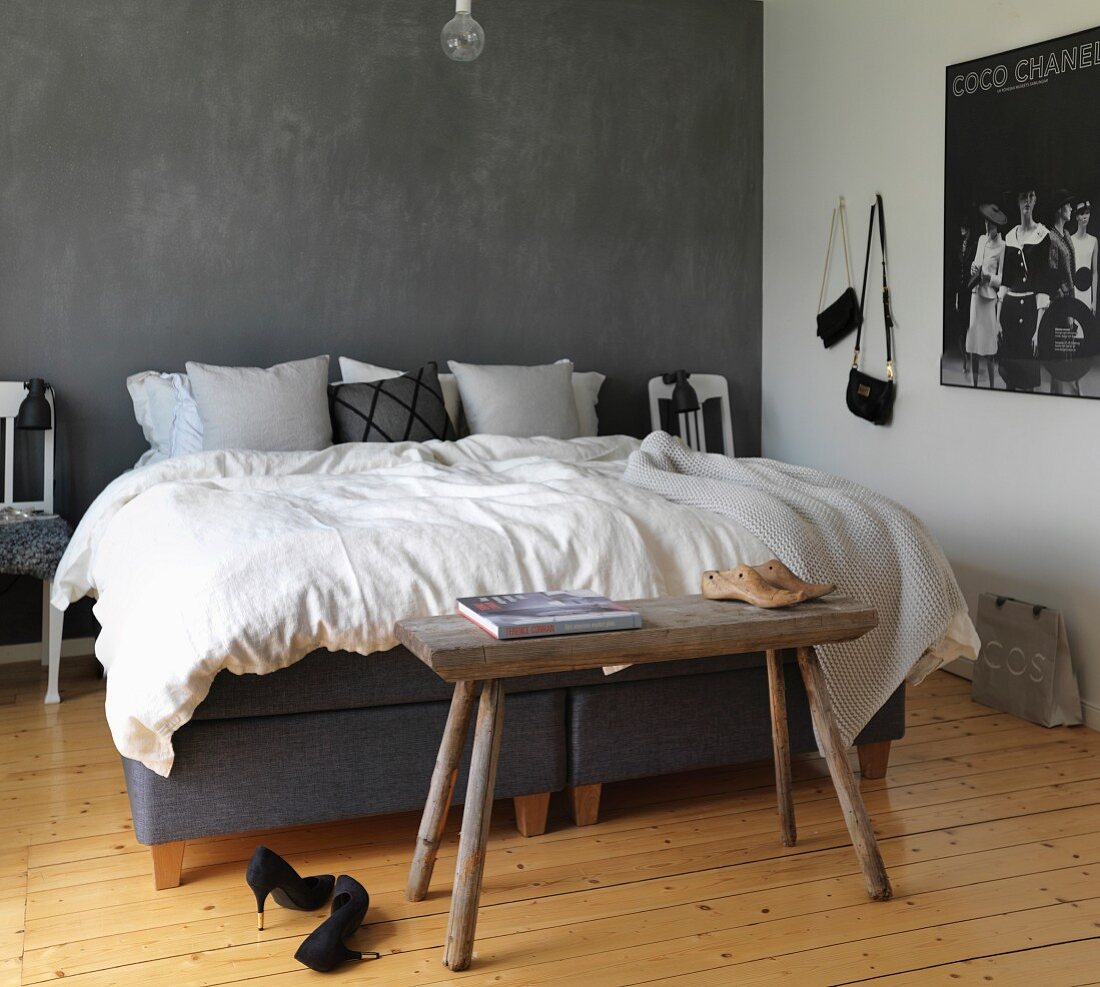 Double bed against grey wall, natural wooden floor and rustic bench in bedroom