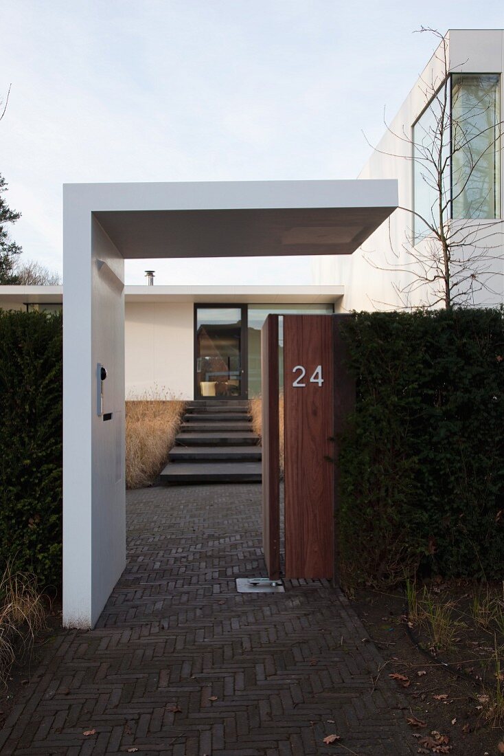 Contemporary house with minimalist modern roof over open garden gate and stone steps leading to front door in background