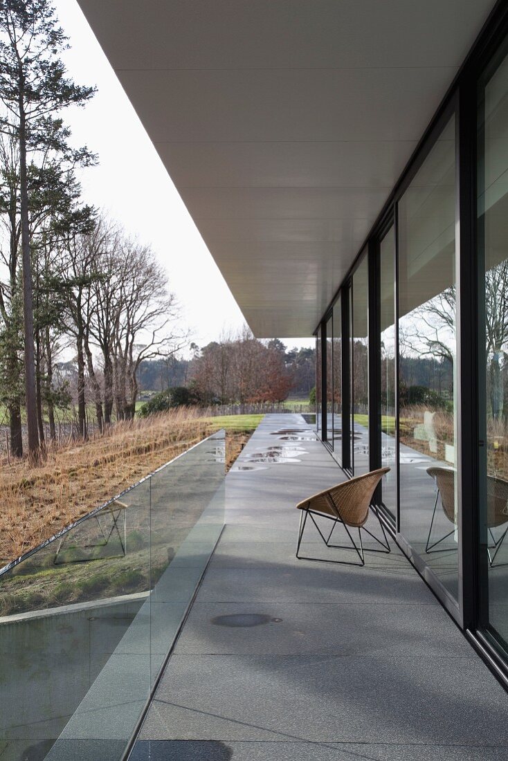 Retro chair on elongated concrete terrace adjoining contemporary house in autumn landscape