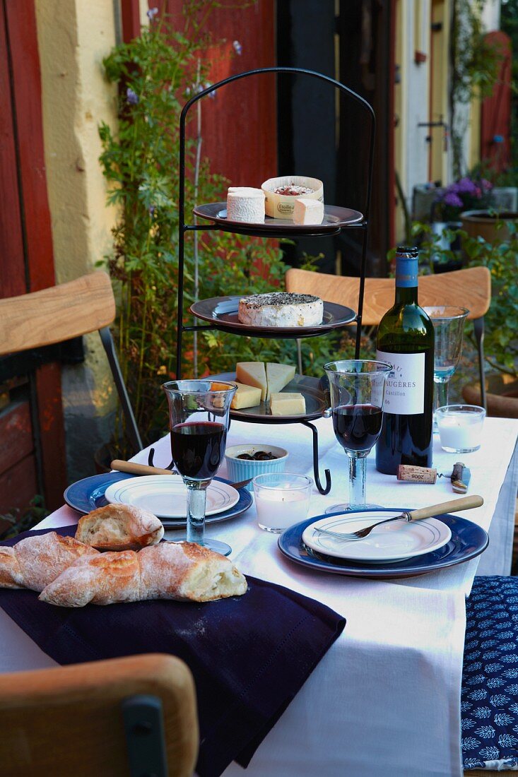Gedeckter Tisch mit Rotwein, Baguette und Käse-Etagere auf der Terrasse
