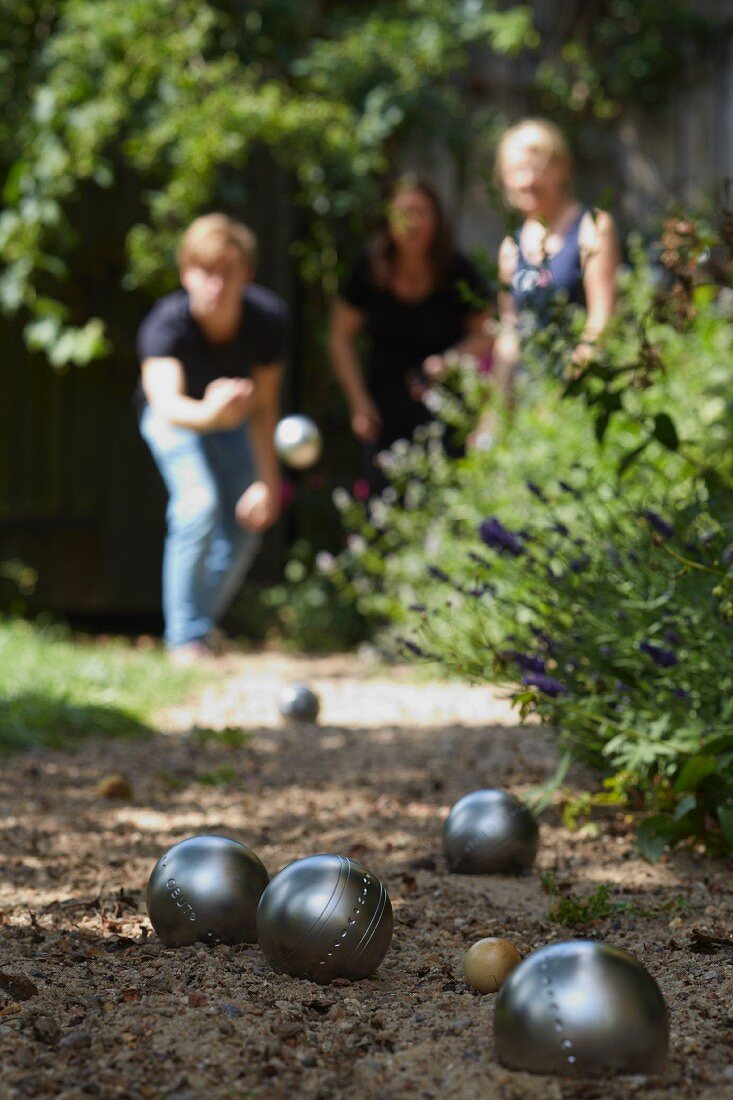 Boules balls on a sandy path in a garden with the players out of focus in the background