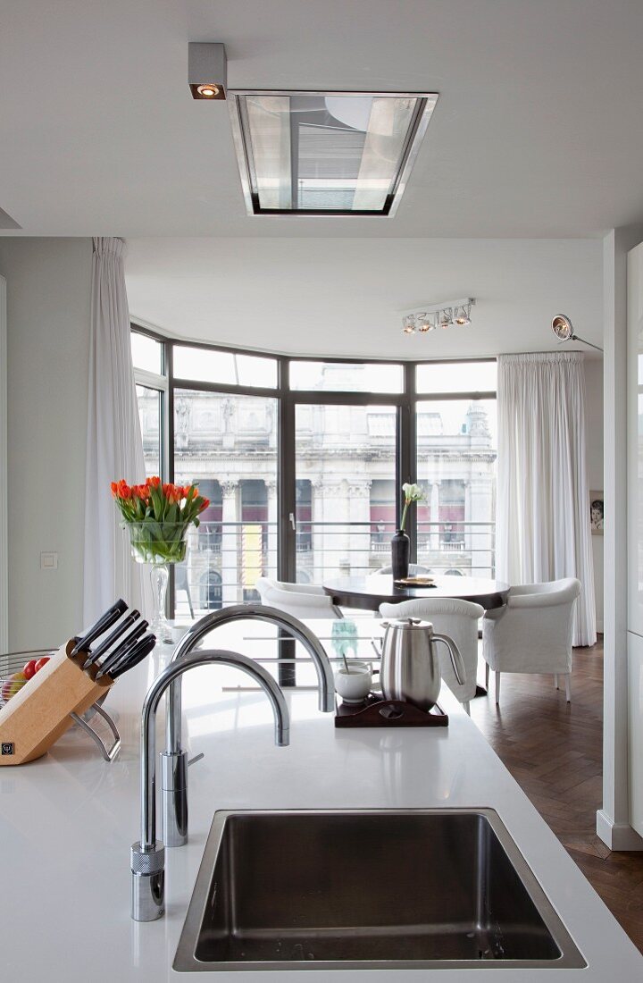 Moderne Kücheninsel mit weisser Arbeitsplatte und eingebauter Spüle, im Hintergrund gediegener Essplatz im Erkerbereich