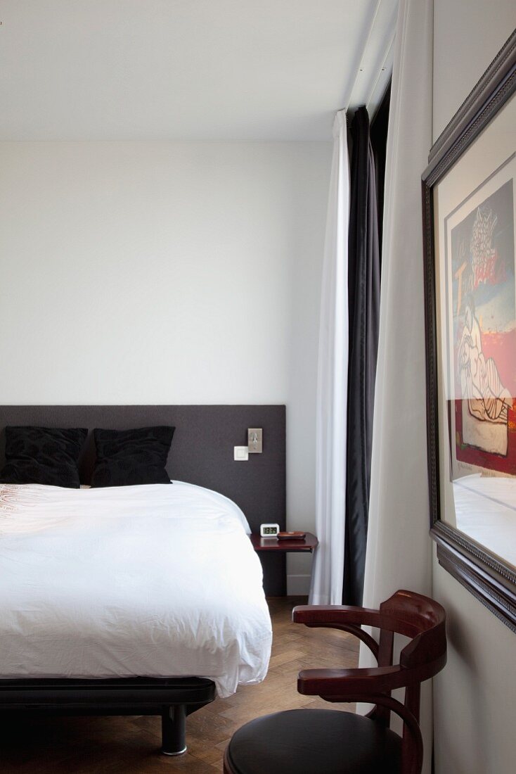 Thonet Armlehnstuhl an Wand und schlichtes Doppelbett in minimalistischem Schlafzimmer