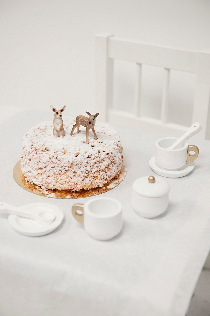 Nut cake decorated with icing sugar and animal figurines on child's table with dolls' tea set