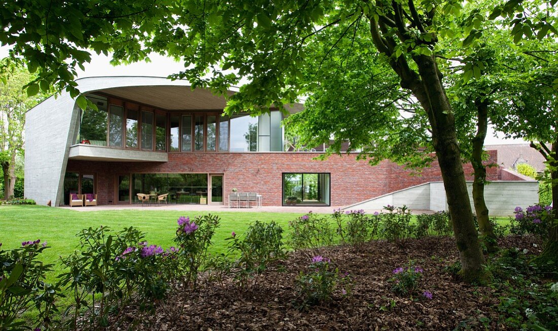 Idiosyncratic house with enclosing concrete facade, glass upper walls and brick-clad lower storey facing park-like gardens