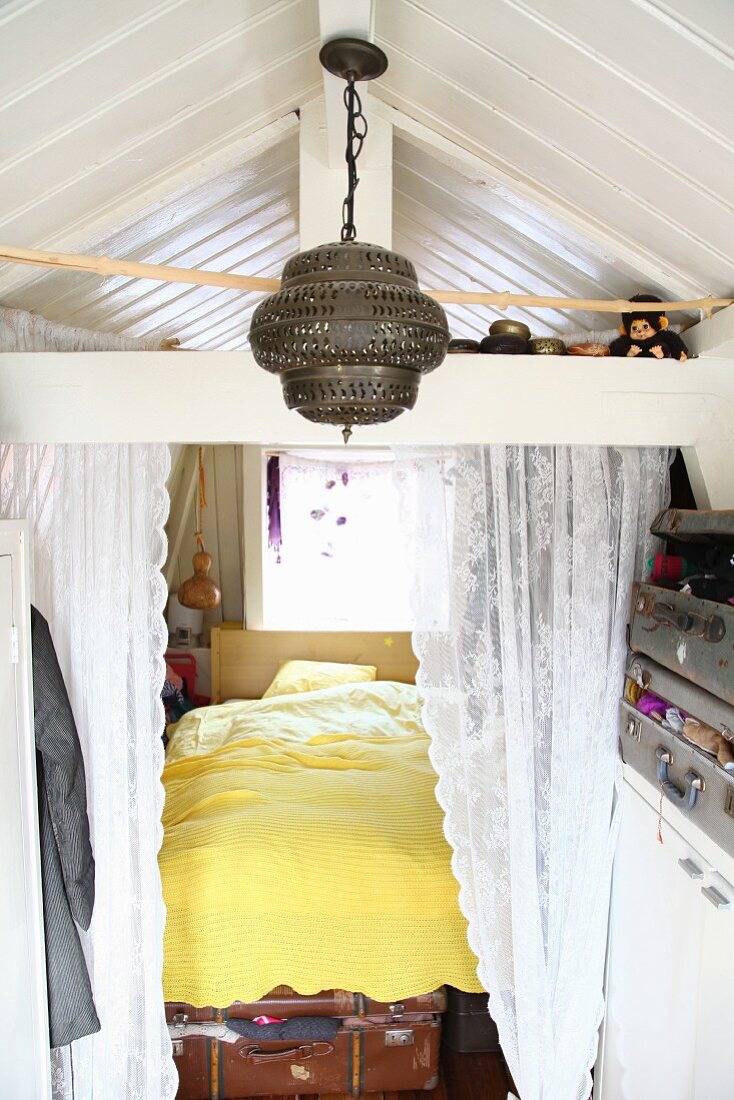 Eingebautes Bett mit Spitzenvorhang, davor orientalische Hängeleuchte und Aufbewahrung in Vintage Koffern