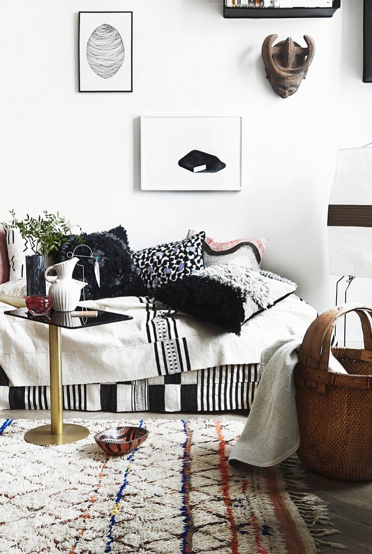 Sofa mit Decken und selbstgestalteten Kissen in Schwarz-Weiß, davor heller, gemusterter Wollteppich