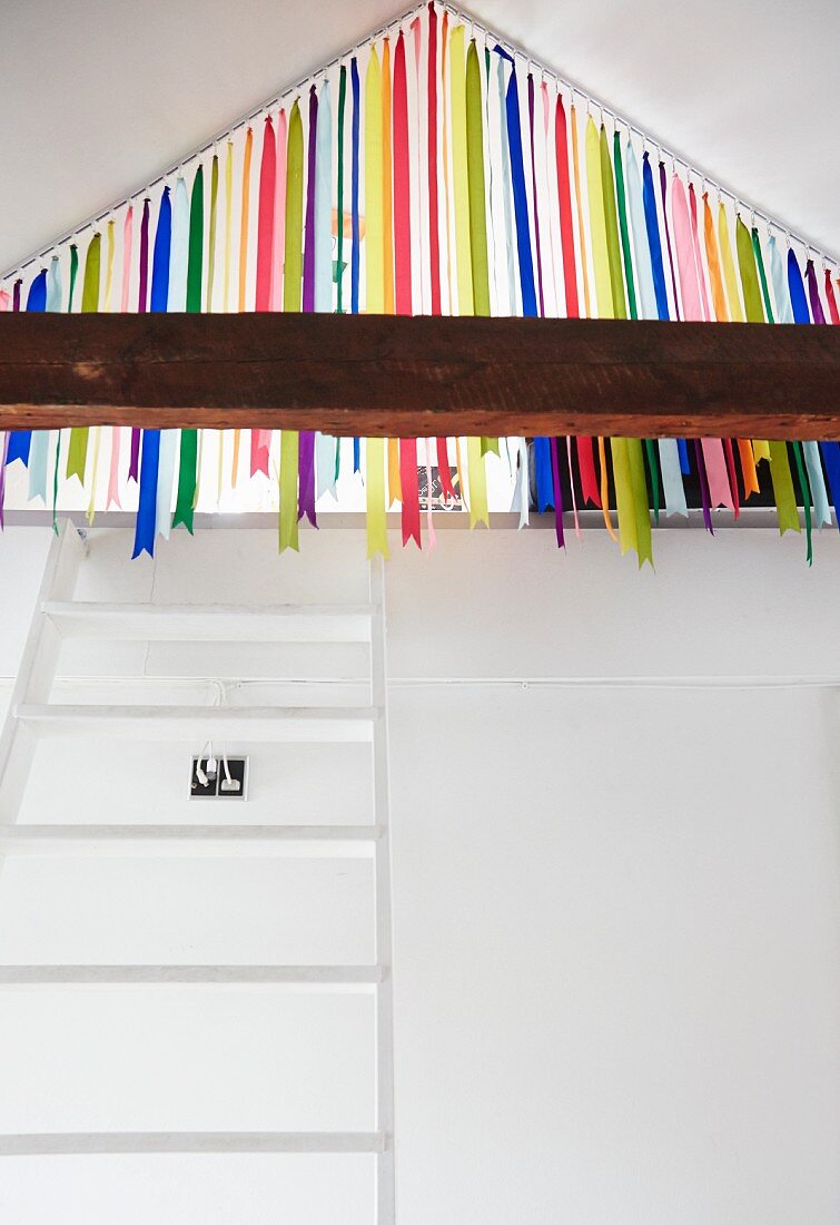 White ladder leading to gallery in attic with colourful ribbon curtain screening entrance