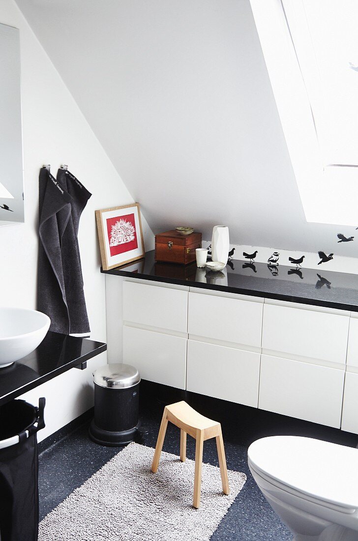 Modern, white bathroom with fitted cabinets under sloping ceiling with bird wall stickers and black accessories