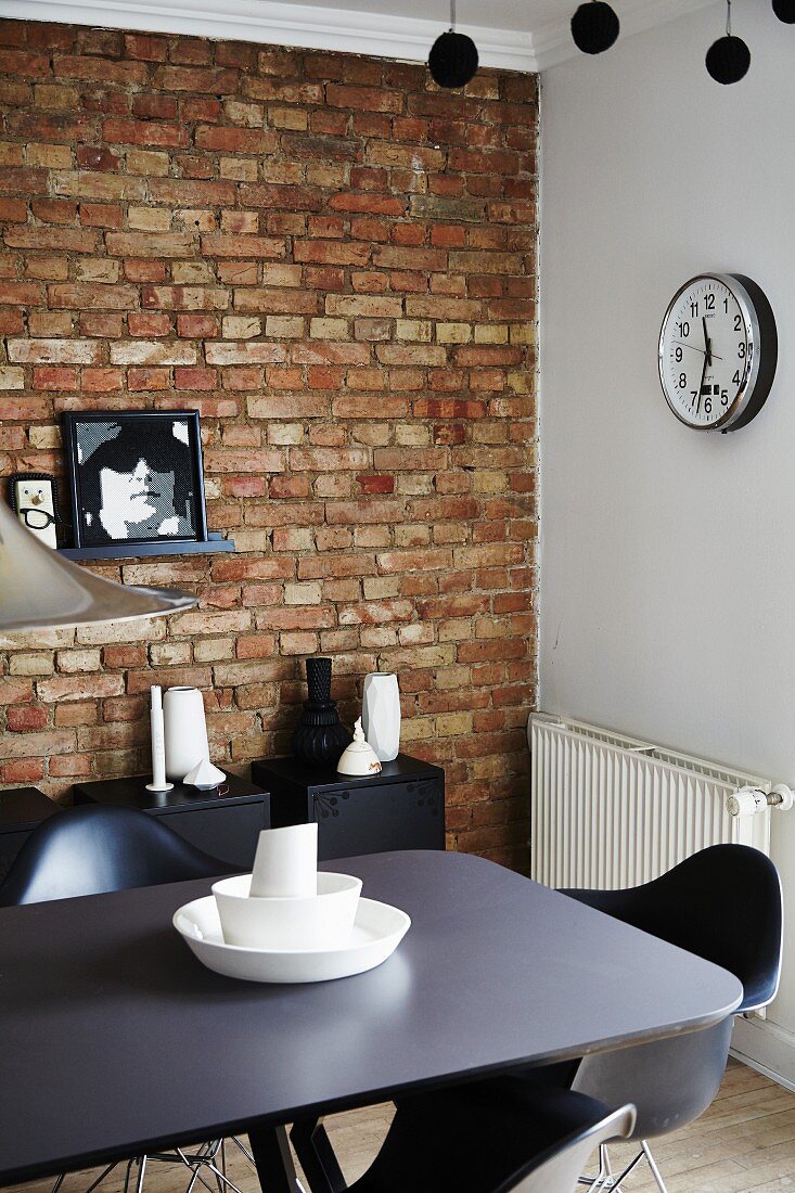 Station clock, unrendered brick wall, black designer furniture and white vases in dining room
