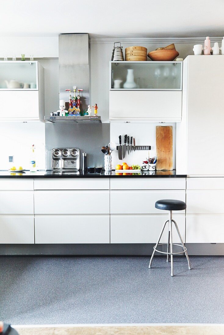 Utensils and wall cabinets in white fitted kitchen with retro barstool
