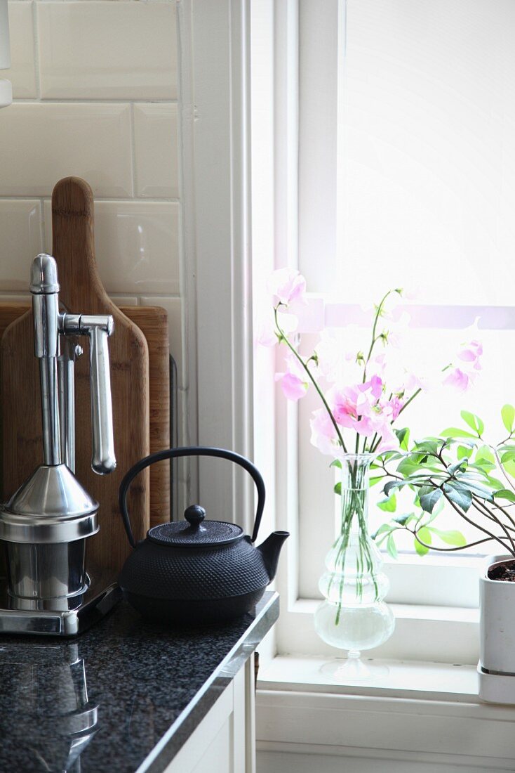 Zarte Blüten und Grünpflanze am Fenster, daneben Zitruspresse und Teekanne auf Küchenarbeitsplatte