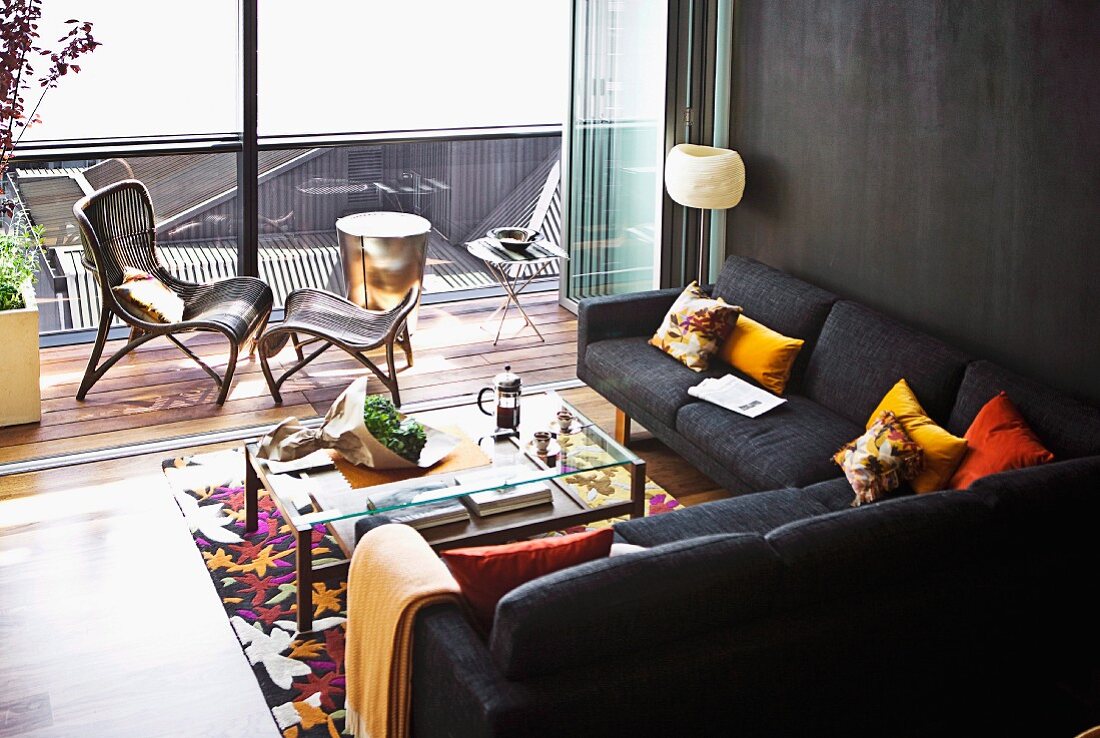 Kissen und Teppich als Farbkontrast zu dunkler Sofalandschaft und Wandgestaltung, im Hintergrund Balkon und geöffnete Faltschiebetüren